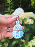 Handmade blue fish dangle earrings held up against a garden background