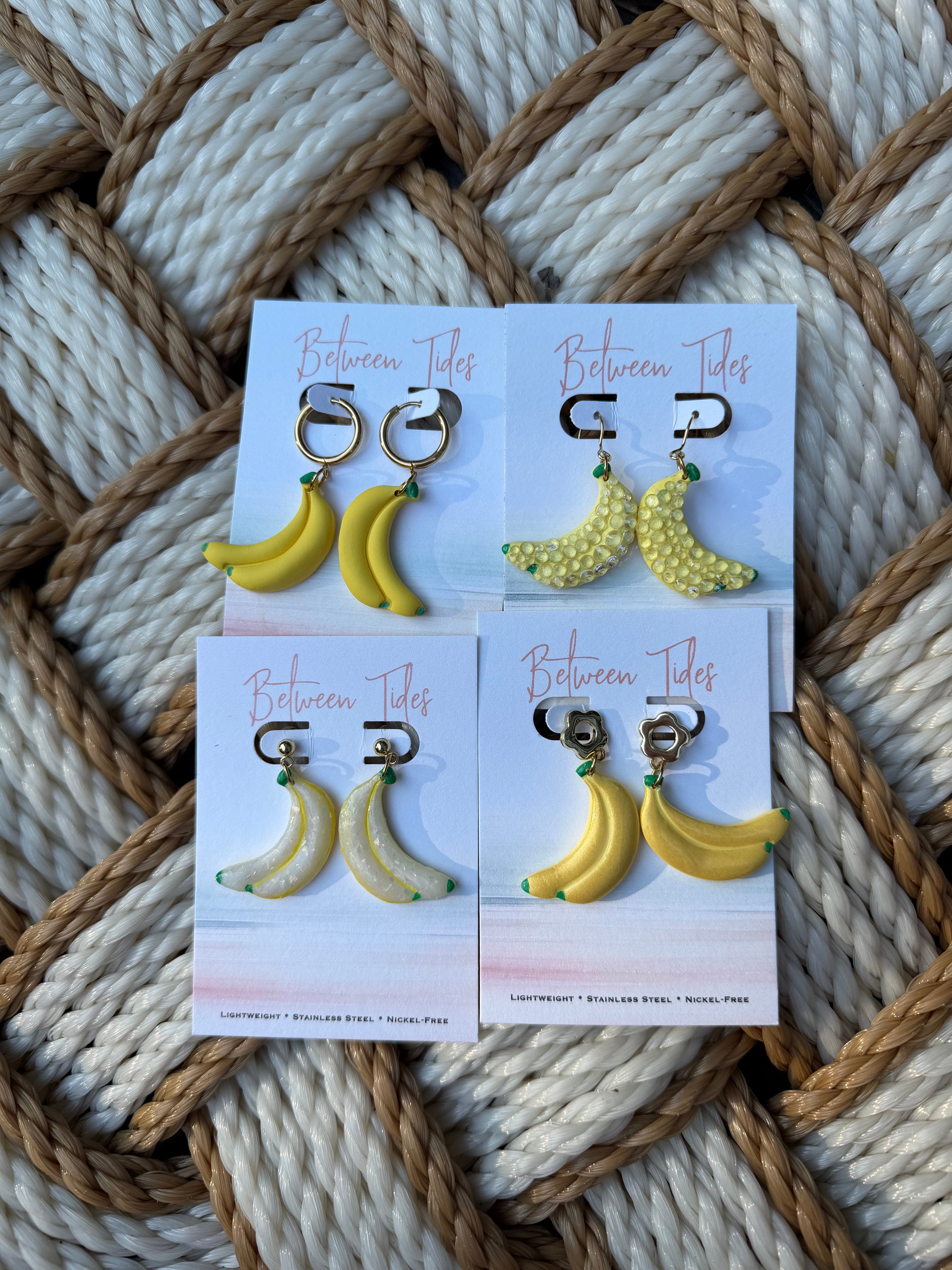 Four styles of banana dangle earrings displayed on Between Tides branded cards
